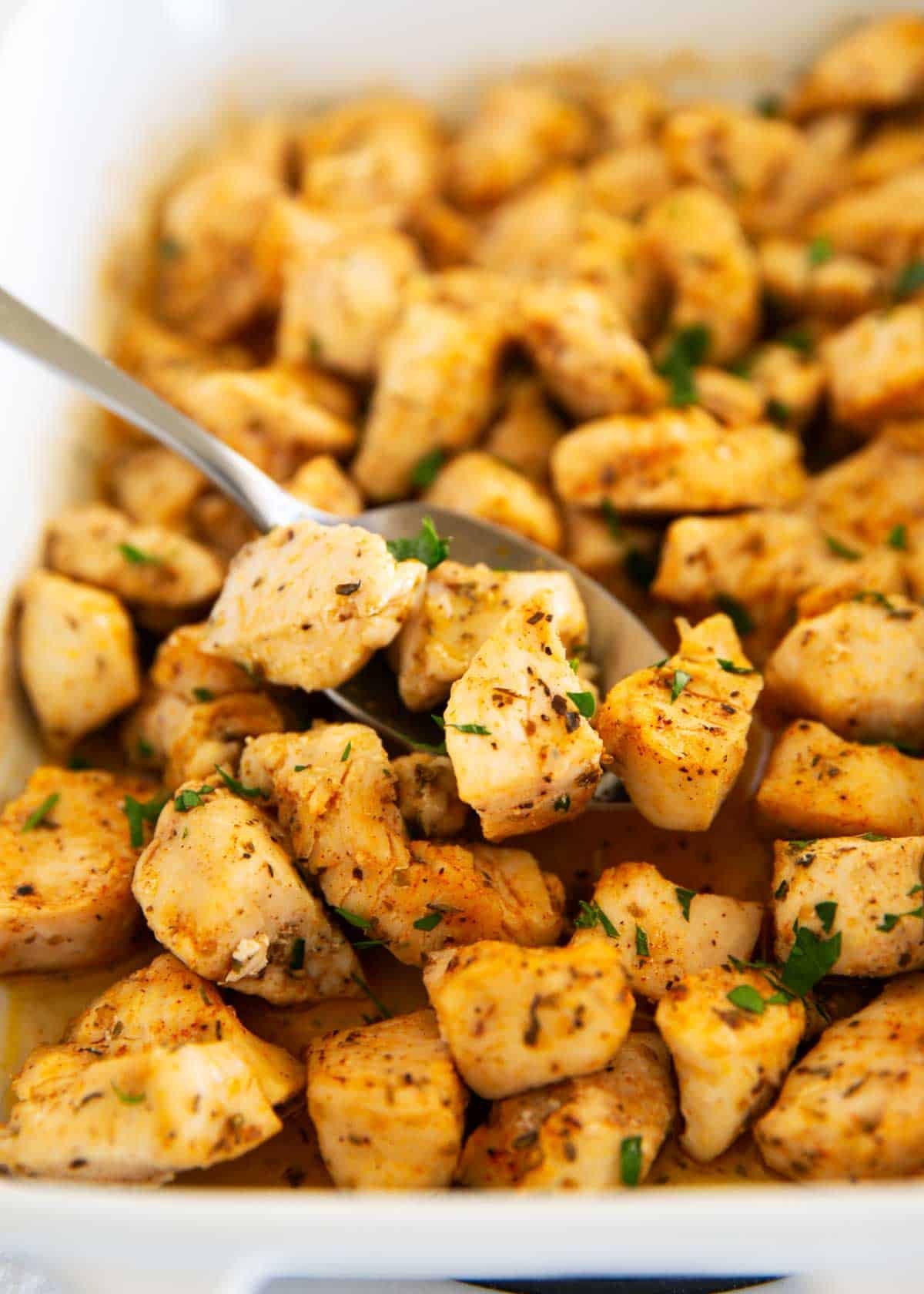 Perfectly seasoned, juicy baked chicken bites are an easy weeknight meal you can throw together in only 20 minutes. This family-friendly dinner can be served in a variety of ways! Baked chicken bites in baking dish with serving spoon.