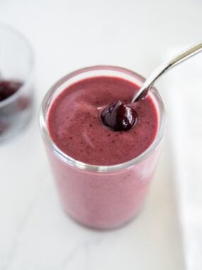 Banana cherry smoothie in a glass cup garnished with a sweet dark cherry.