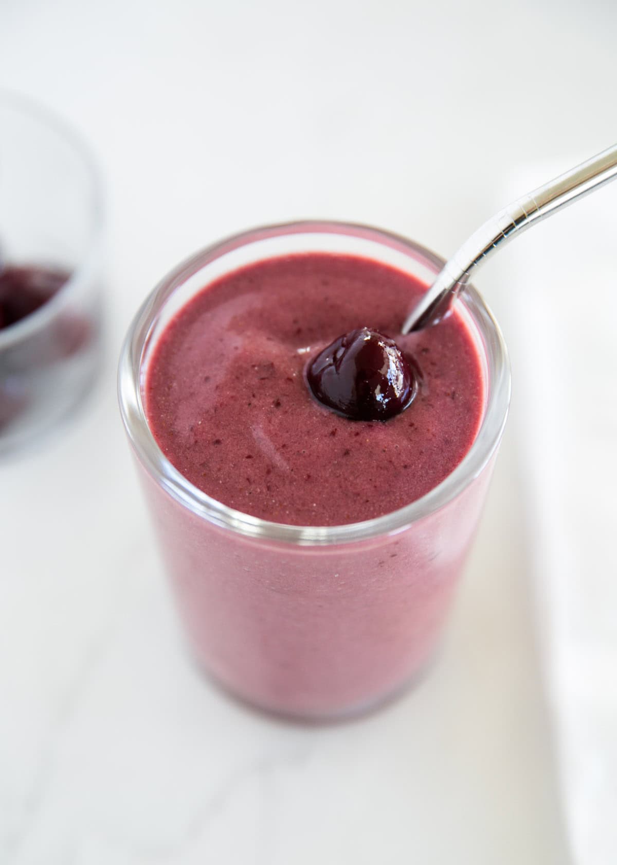 Sweet cherries, frozen bananas, and almond milk blended into a creamy cherry smoothie that is vibrant and refreshing! The perfect pick-me-up anytime of the day. Cherry smoothie in a glass cup.