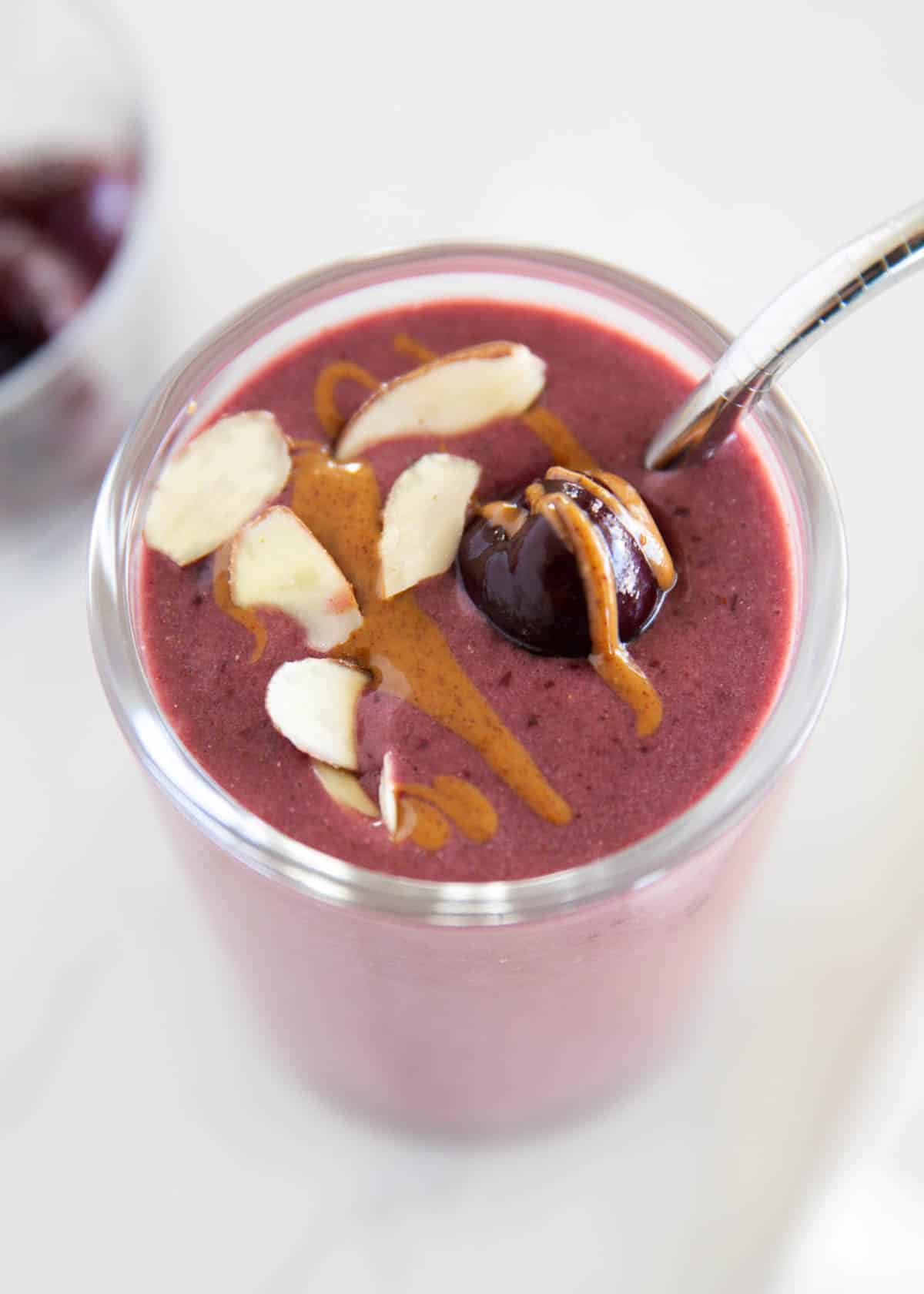 Sweet cherries, frozen bananas, and almond milk blended into a creamy cherry smoothie that is vibrant and refreshing! The perfect pick-me-up anytime of the day. Banana cherry smoothie in a glass cup garnished with a fresh cherry, almonds and a drizzle of almond butter.