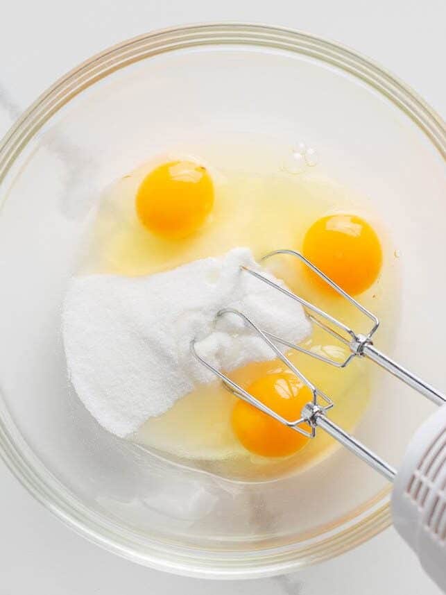Eggs and sugar in a bowl with electric mixer.