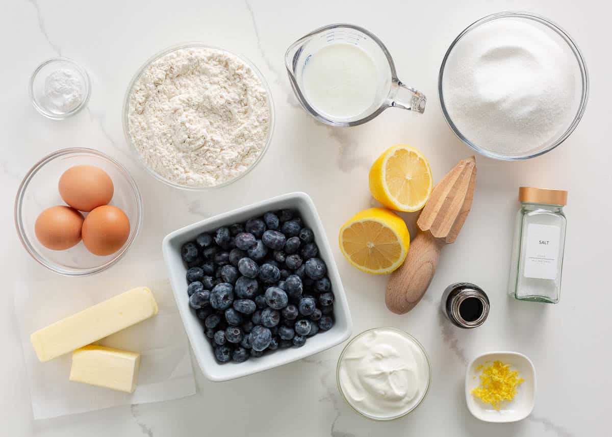 Lemon, blueberries, eggs, sugar, flour, sour cream, buttermilk and butter on counter.