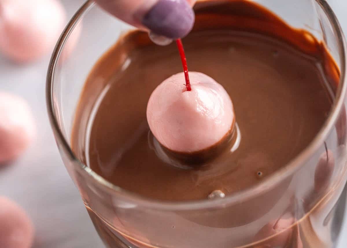 Dipping a homemade chocolate covered cherry into melted chocolate for a smooth outer coating.