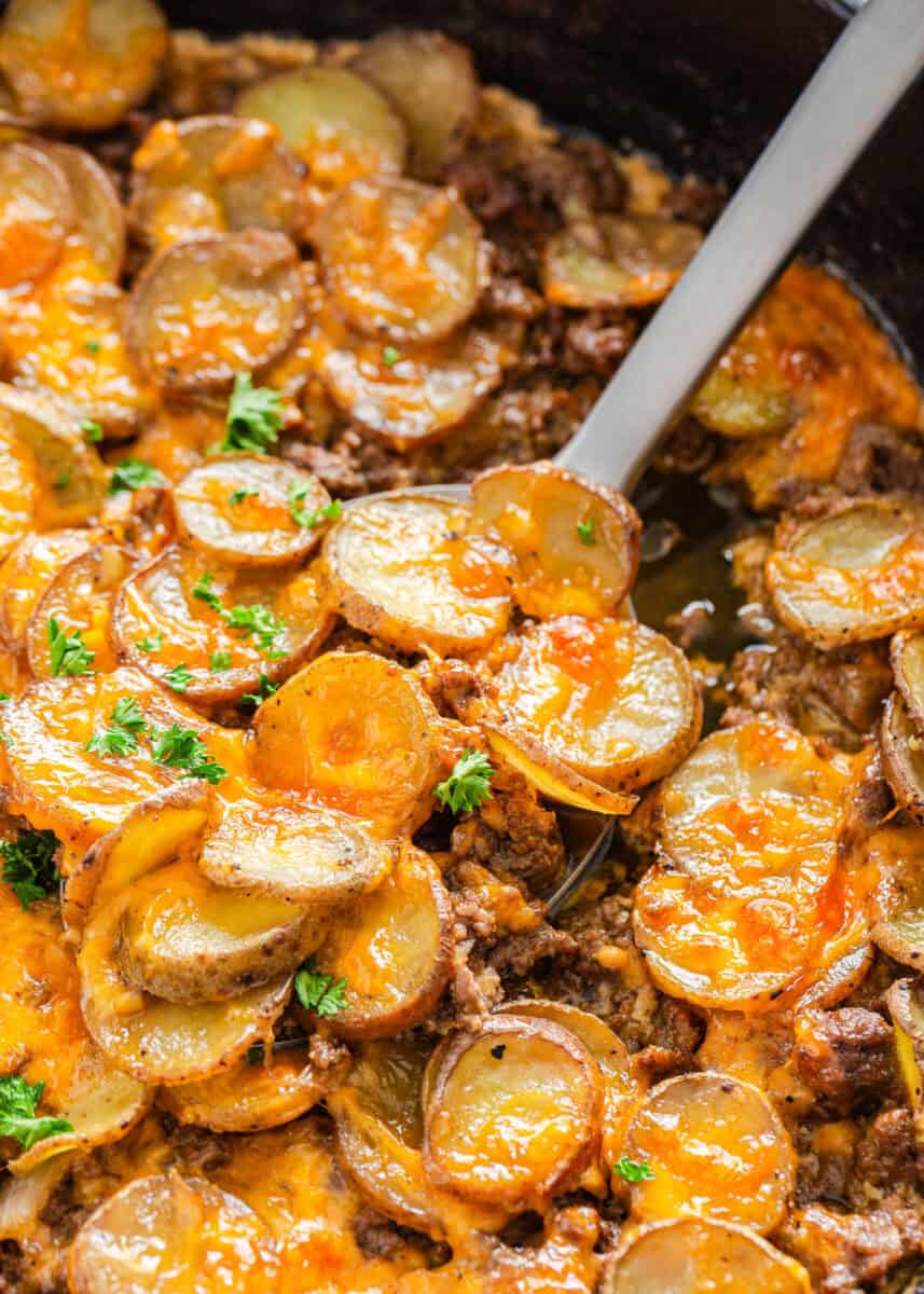 Ground beef and potatoes in a skillet with spoon. This easy weeknight dinner is hearty with ground beef, potatoes and cheese.