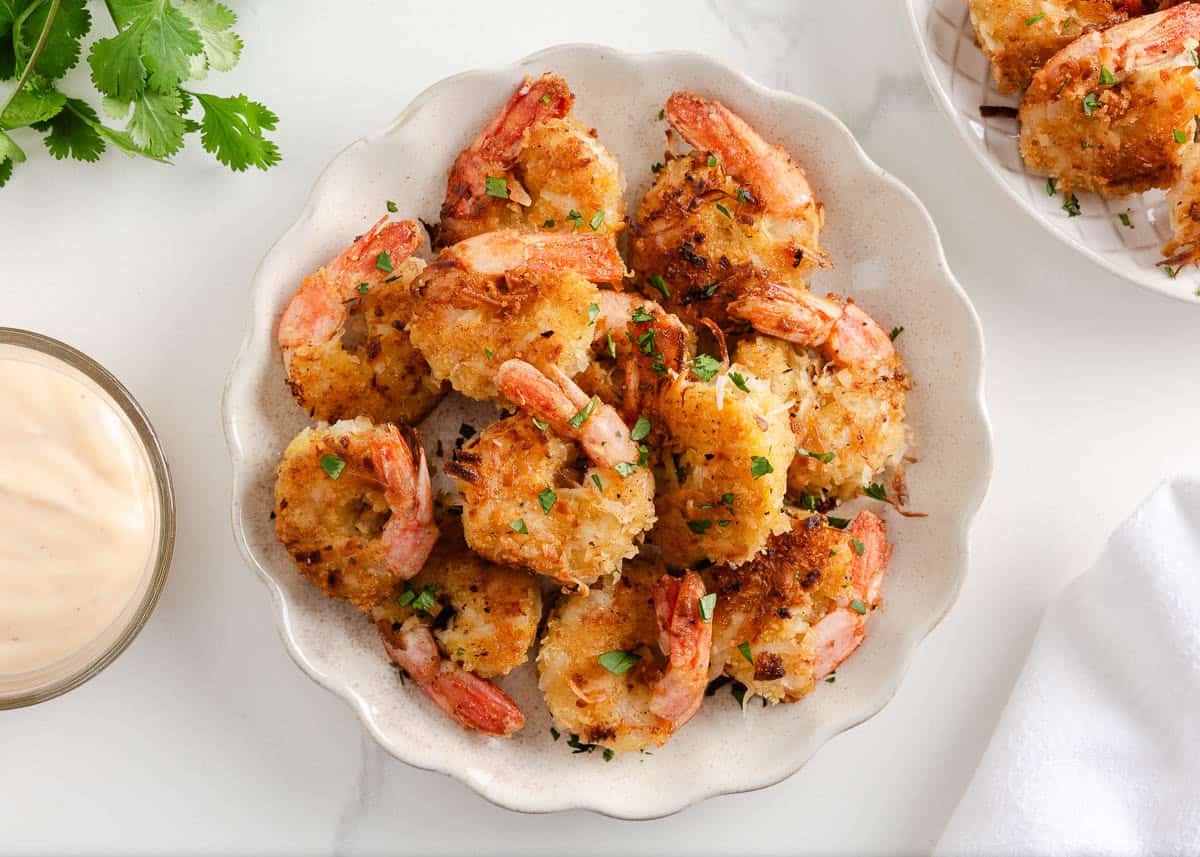 Coconut shrimp on a plate with dipping sauce nearby.