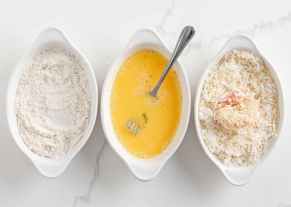 Showing process of dipping shrimp into flour, egg and coconut.