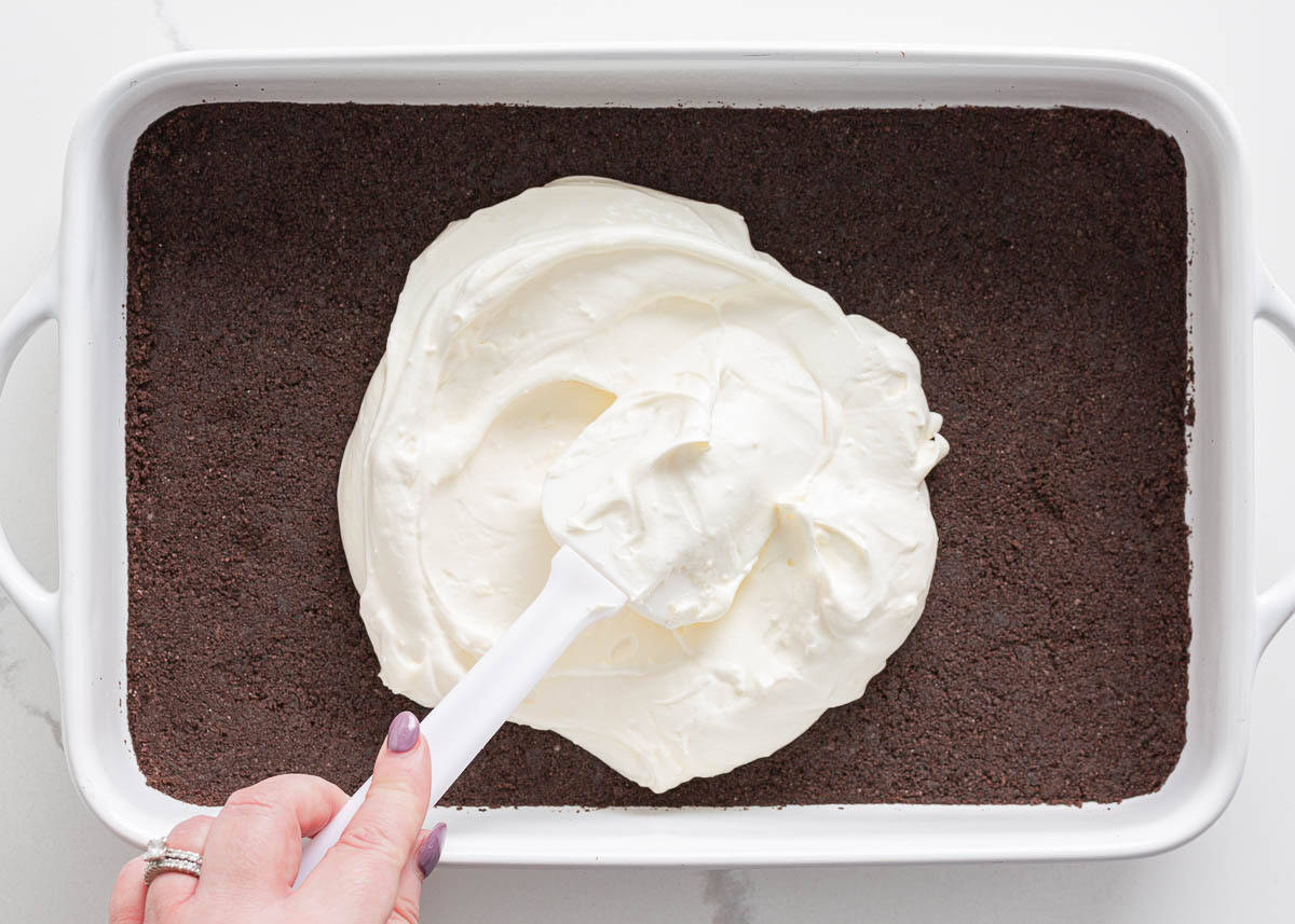 Spreading the cream cheese and whipped topping layer over an Oreo cookie crust in a 9×13 dish.