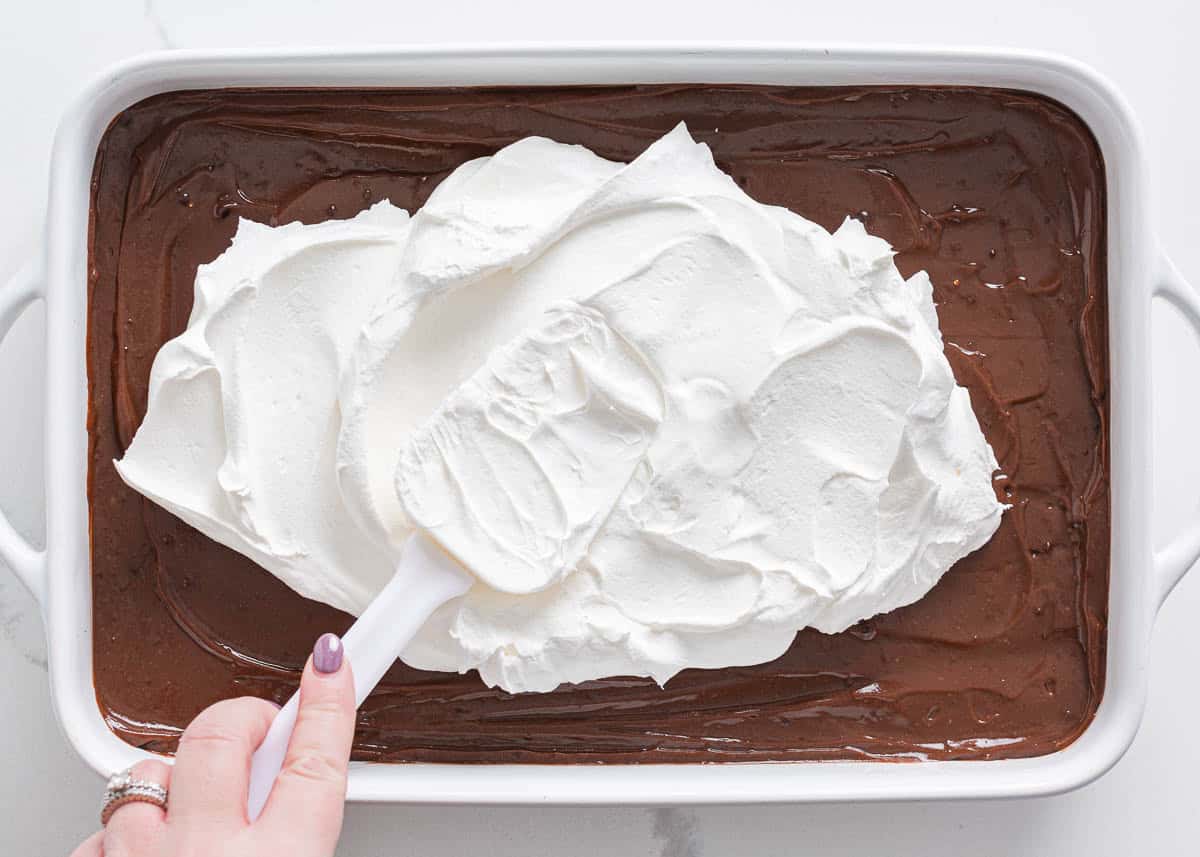 Adding whipped topping over the chocolate pudding layer for Easter dirt cake.
