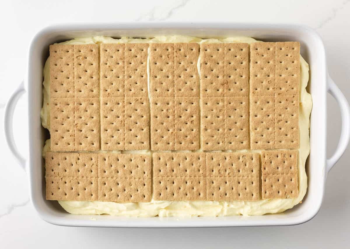 Layer of graham crackers placed over vanilla pudding filling for eclair cake with chocolate ganache.