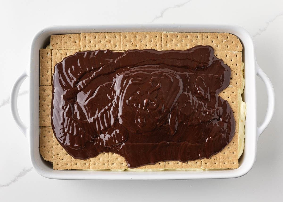 Chocolate ganache spread over eclair graham cracker layer in a baking dish