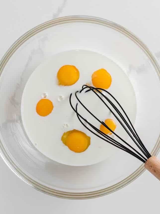 Eggs and whole milk being whisked in a bowl.