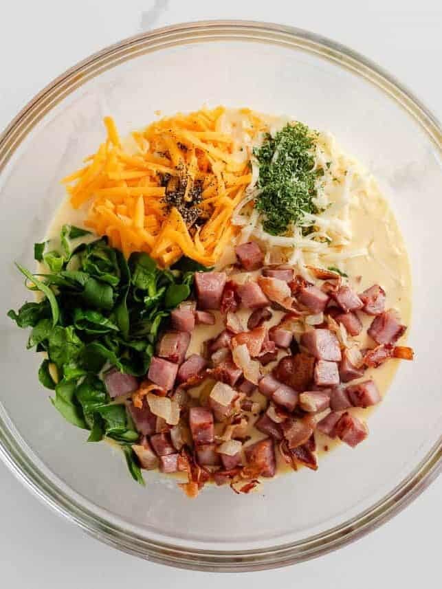 Showing ingredients for ham and cheese quiche in a bowl to mix together.