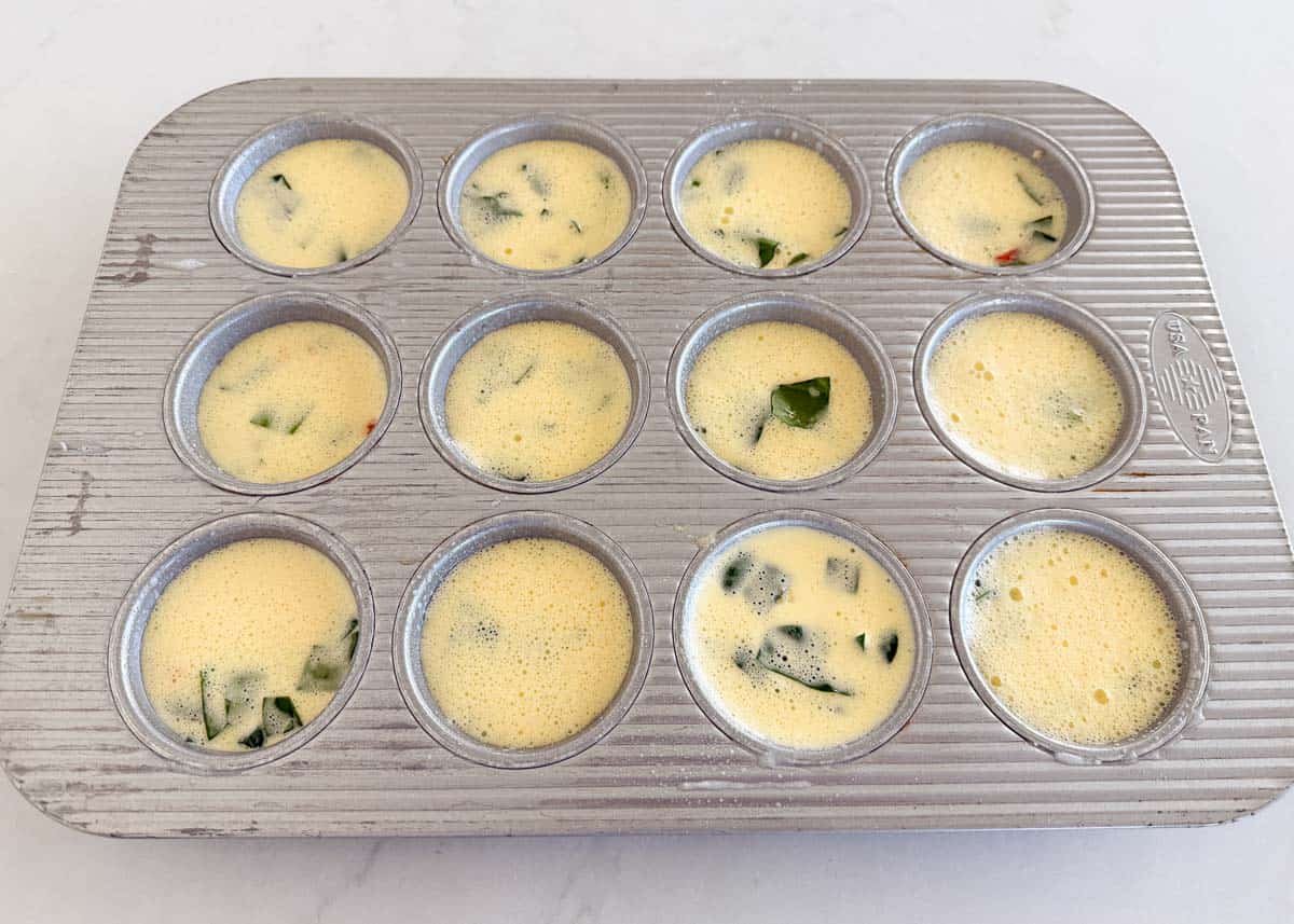 Unbaked cottage cheese egg bite mixture poured into a greased muffin pan before baking.