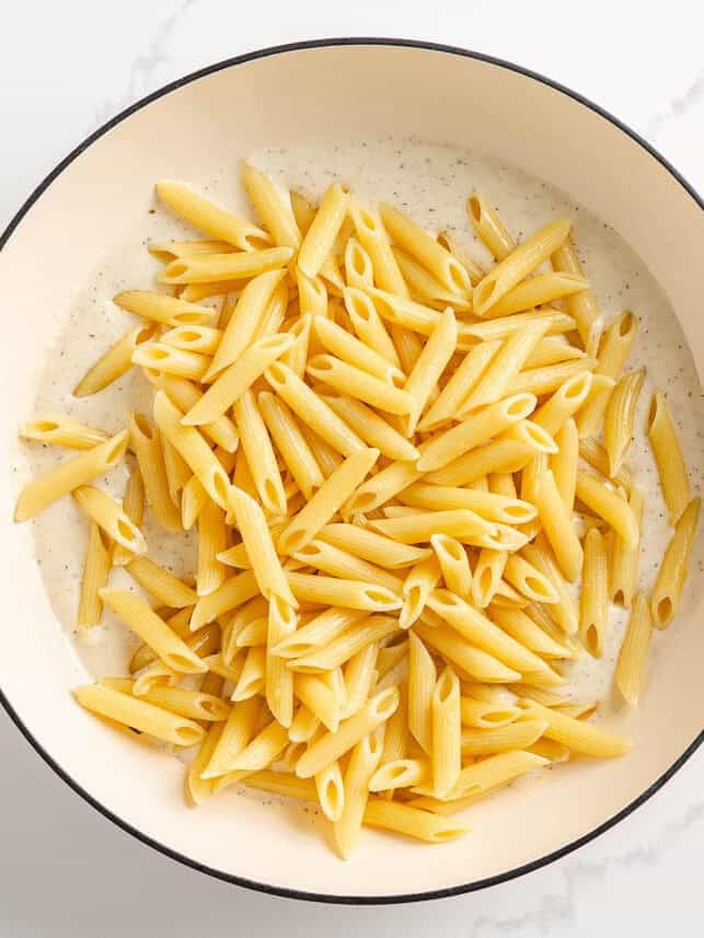 Adding cooked penne pasta into a creamy garlic white sauce.
