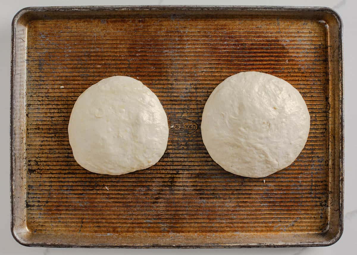 Two sourdough pizza dough balls on a baking sheet.