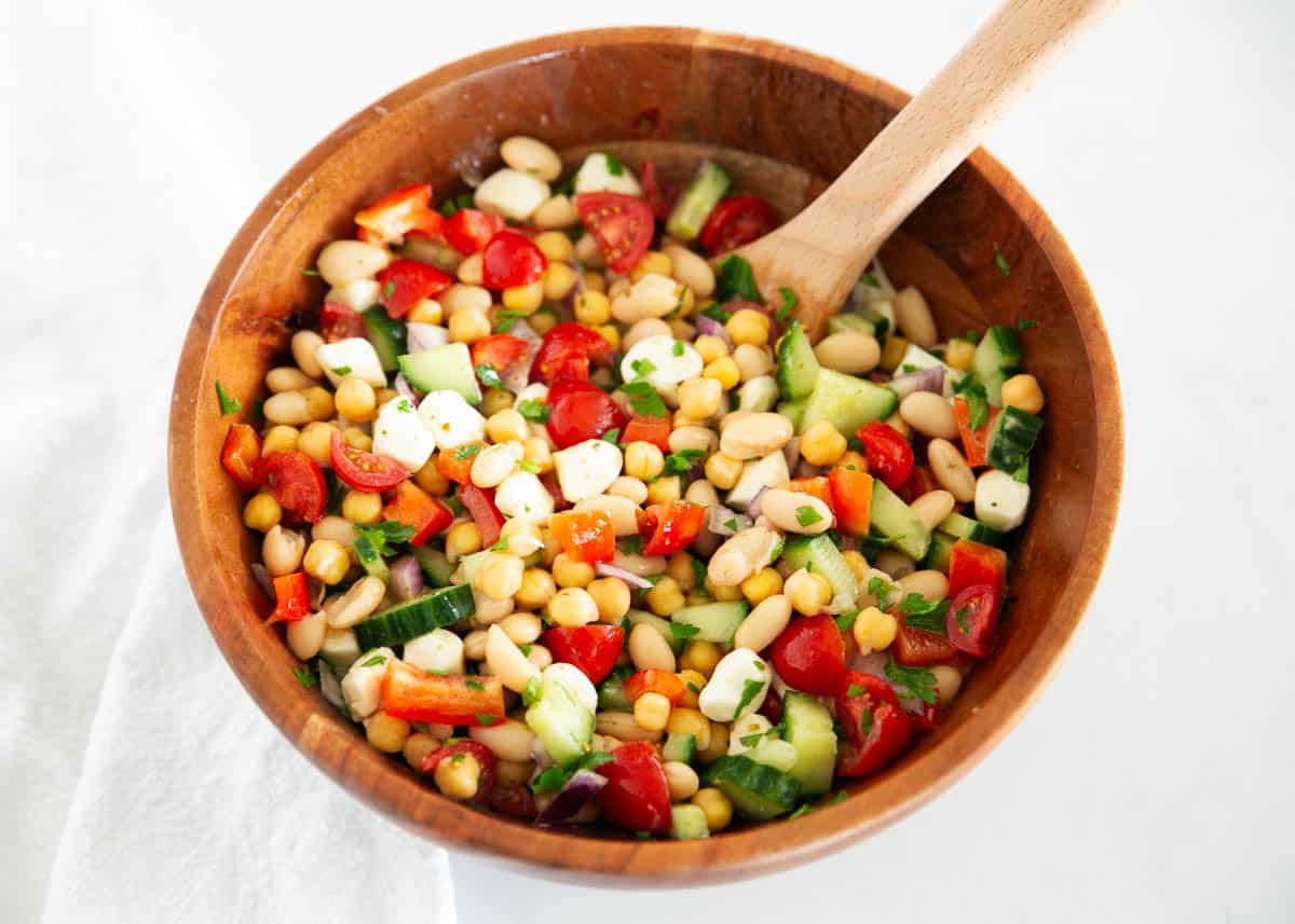 Learn to make this simple, dense bean salad TikTok sensation! It's fresh and healthy, vibrant and colorful, with plenty of crunch, then tossed in a tangy homemade dressing. Dense bean salad in a wooden bowl.