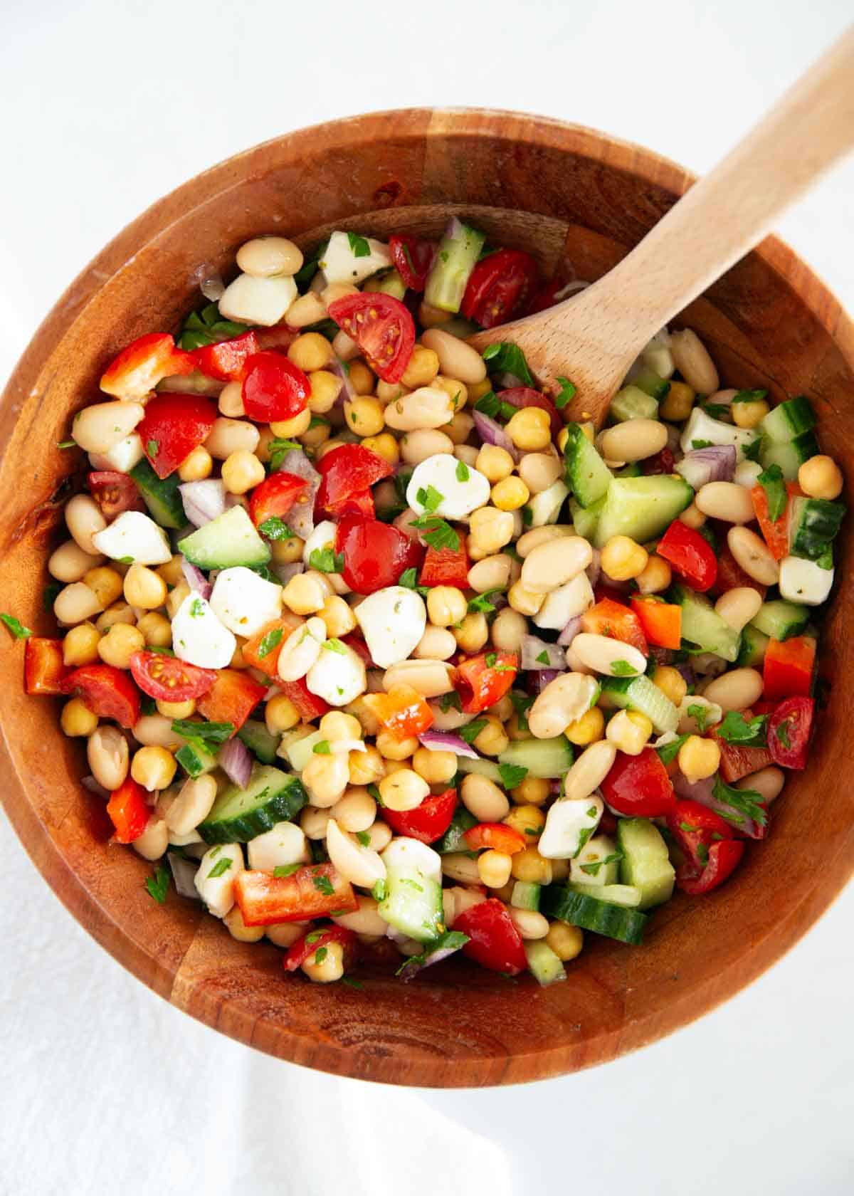 Learn to make this simple, dense bean salad TikTok sensation! It's fresh and healthy, vibrant and colorful, with plenty of crunch, then tossed in a tangy homemade dressing. Dense bean salad in a wooden bowl.