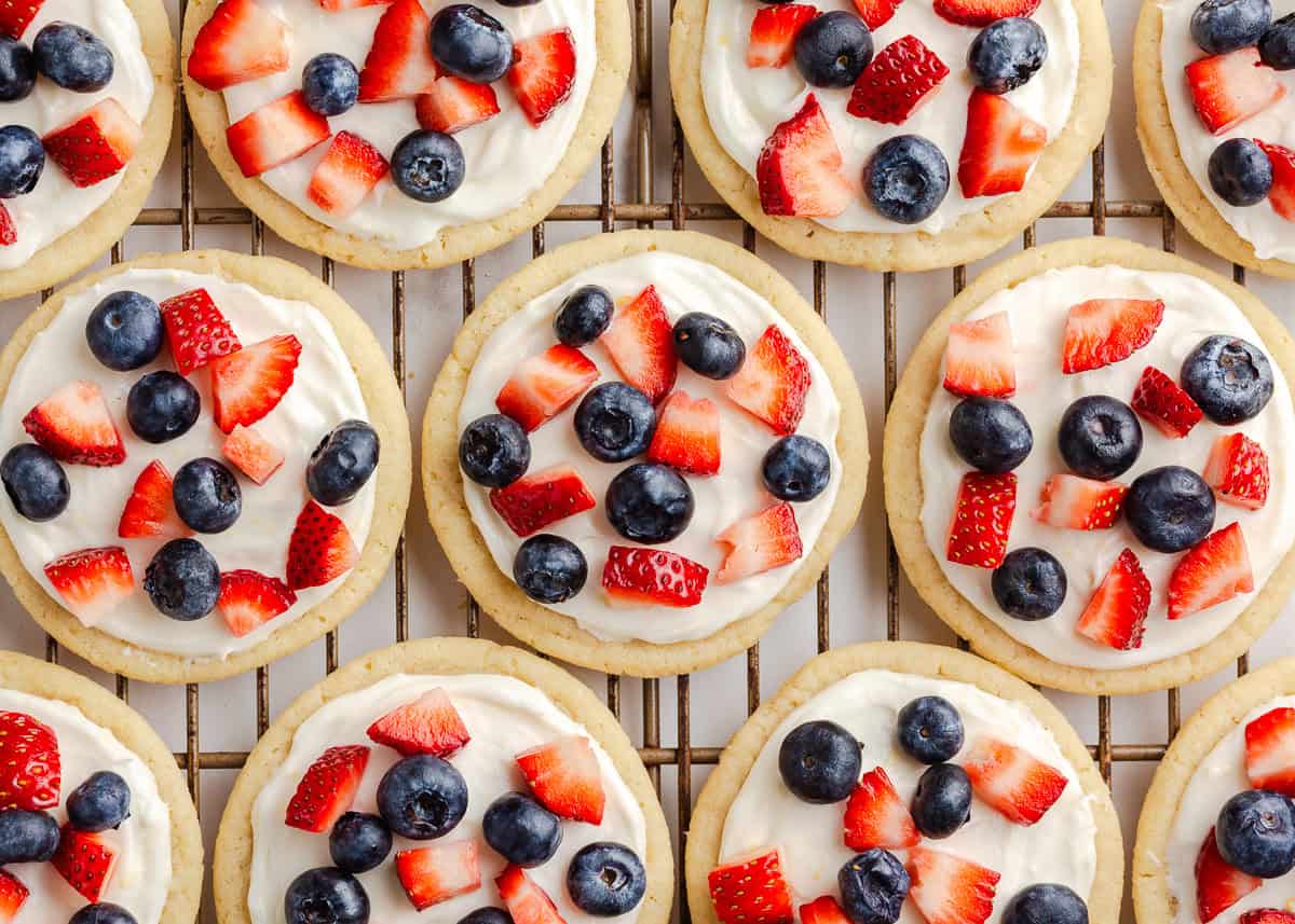 Mini sugar cookie fruit pizzas on wire rack decorated with red, white and blue berries.