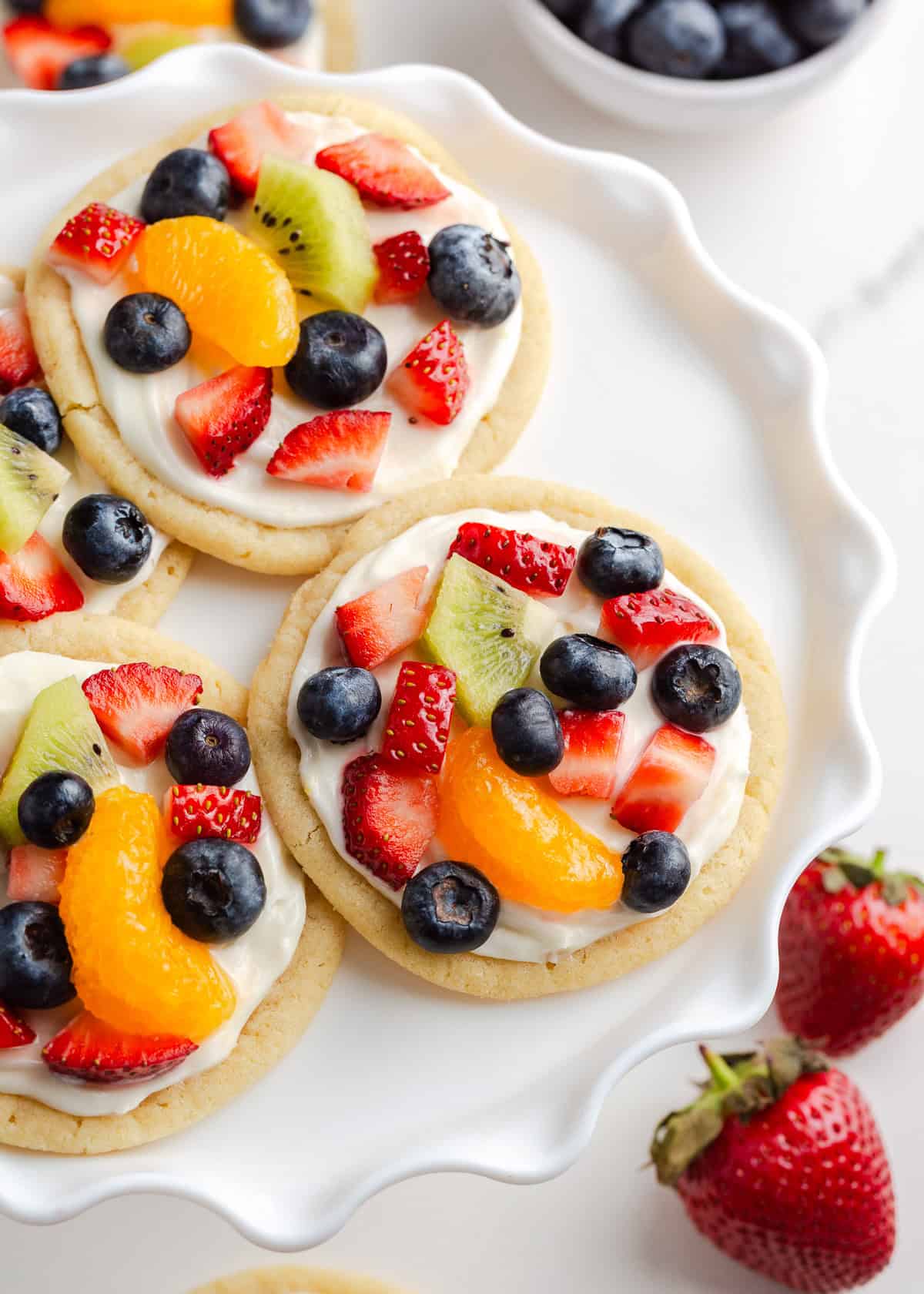 Sugar cookie fruit pizzas on a white fluted dish.