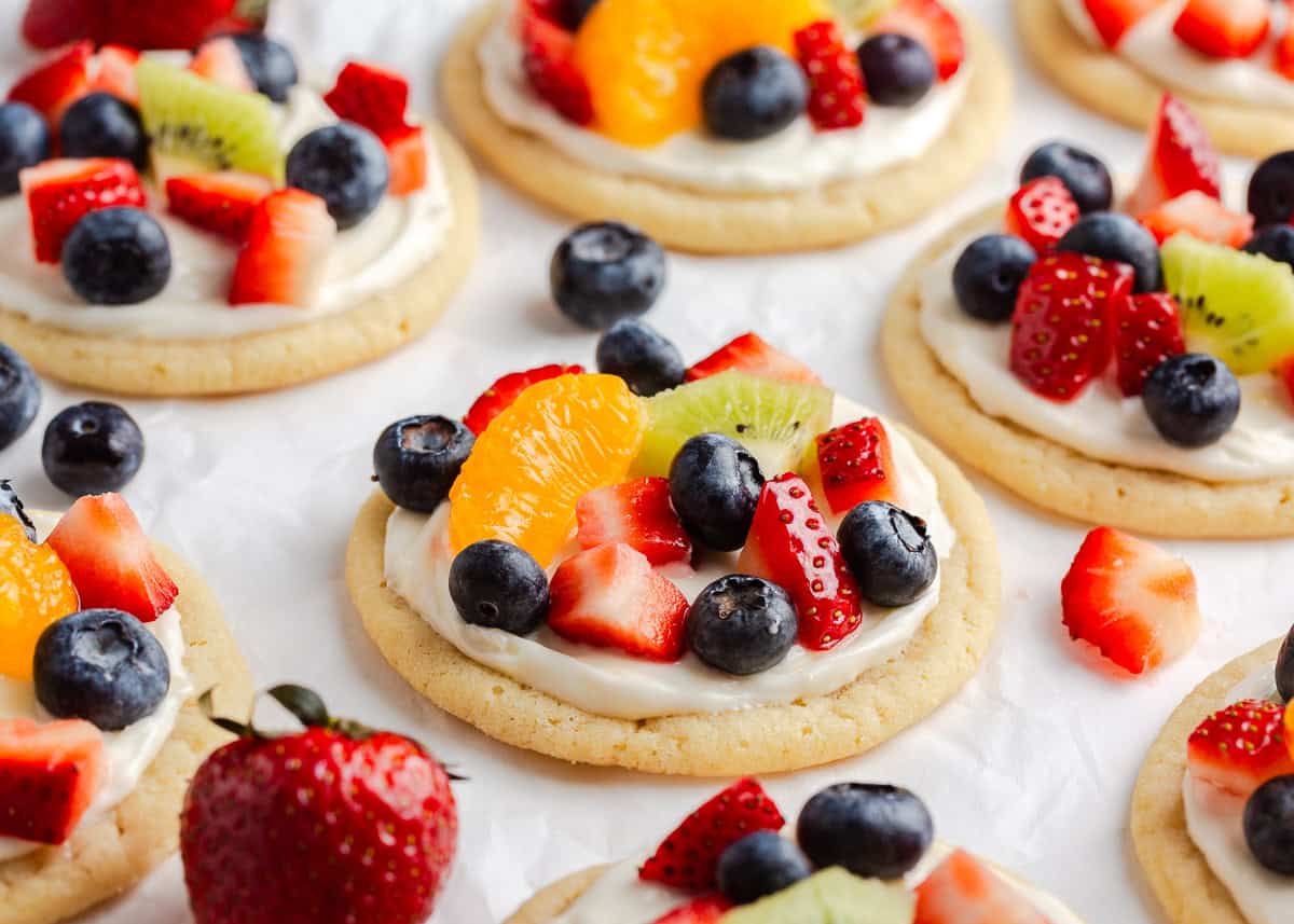 These fruit pizza cookies have a sugar cookie base, cream cheese frosting, and a beautiful assortment of fresh fruit on top. They're fun, vibrant, and so easy to make! Fruit pizza cookies topped with fruit on the counter.