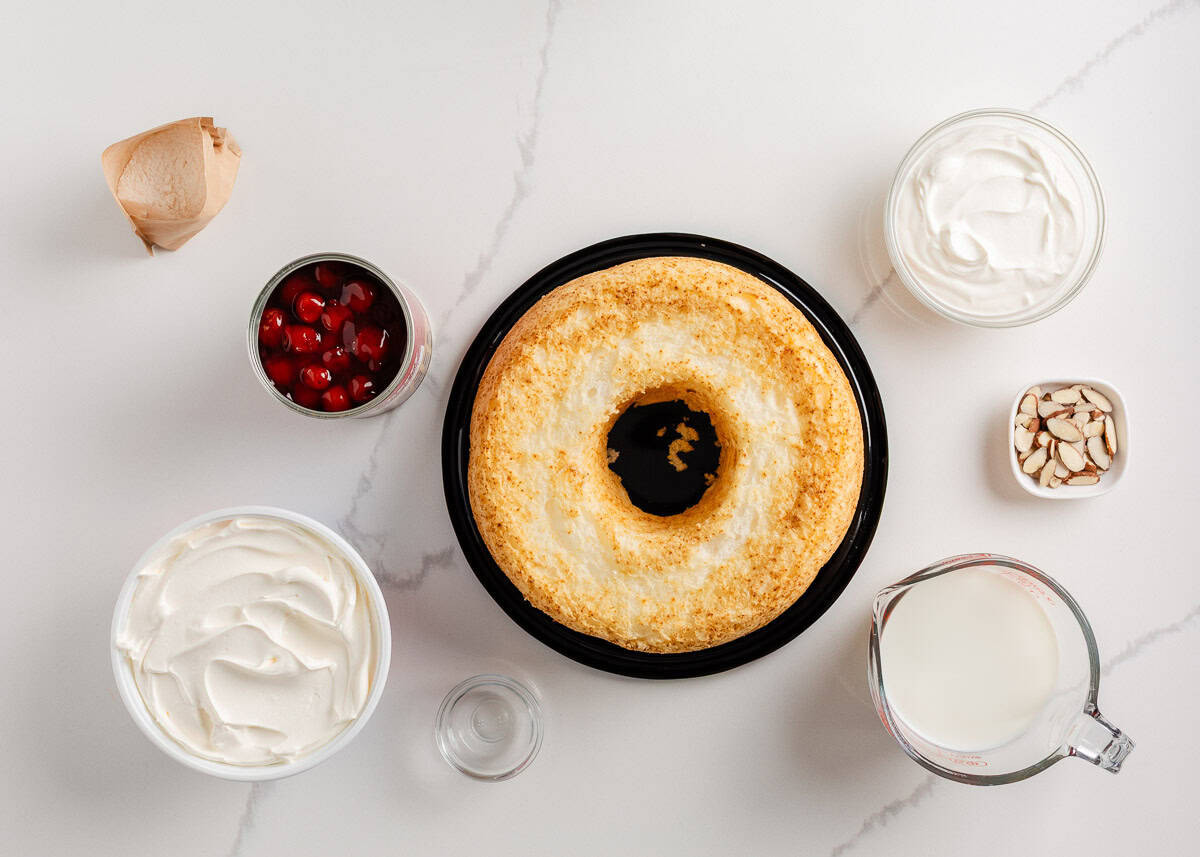 Angel food cake, whipped cream, cherry pie filling, sour cream and sliced almonds on the counter.