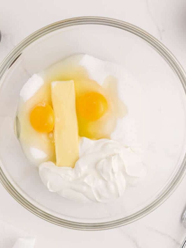 Sour cream, eggs and sugar in glass bowl.