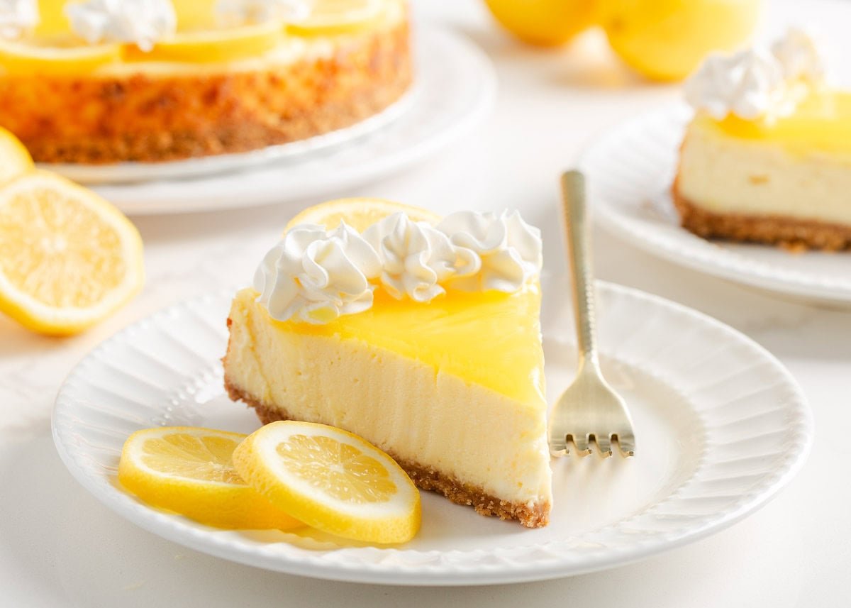 A graham cracker crust is the base for what can only be described as the best baked lemon cheesecake with a layer of lemon curd on top. It's sweet, bright and lemony! A slice of lemon cheesecake on a white plate.
