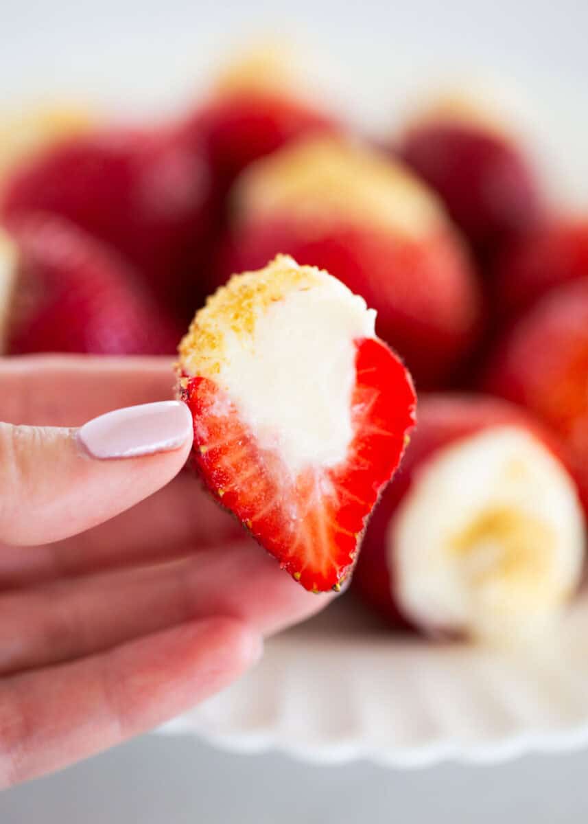 Holding up a strawberry cut in half with cheesecake filling.