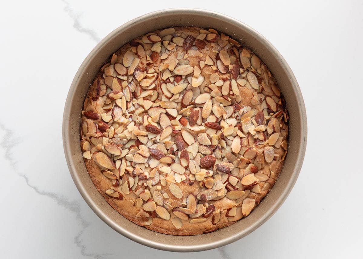 Baked almond torte in a round pan with toasted sliced almonds on top.