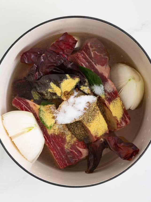 Beef chuck roast, ribs, onion, garlic, carrots, bay leaves, and dried peppers in a Dutch oven with water.