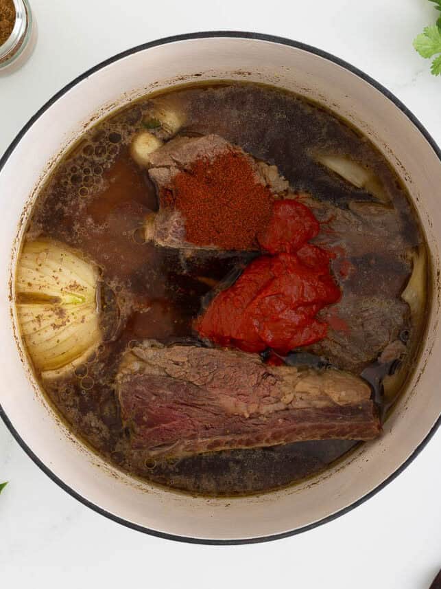 Showing birria in a pot with pureed peppers and chili powder. 