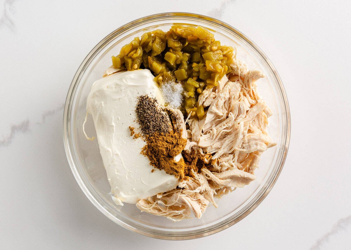 Cream cheese, chicken, spices and green chiles in a bowl.