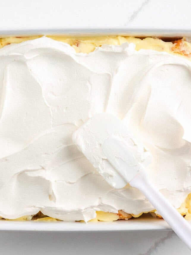 Spreading cool whip on top of cake.
