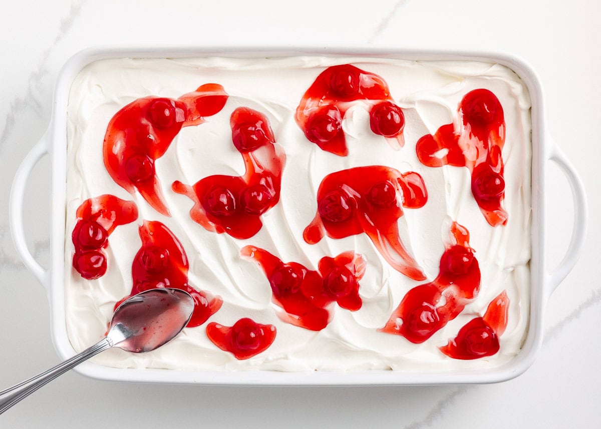 Adding cherry pie filling on top of whipped cream.