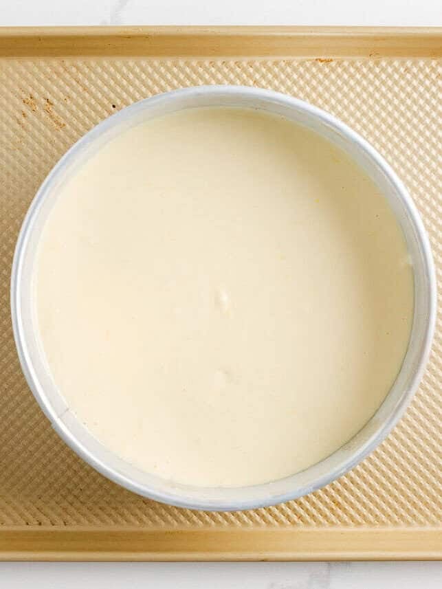 Lemon cheesecake batter in a springform pan on baking sheet.