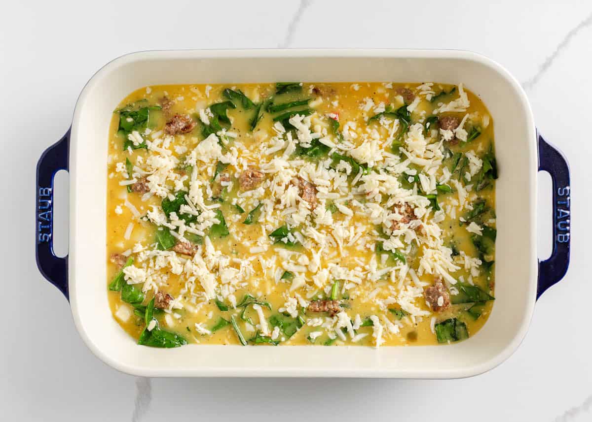 Easy Potatoes O’Brien breakfast casserole in a baking dish with sausage, spinach, eggs and shredded cheese before baking.