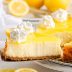 Creamy baked lemon cheesecake slice with lemon curd layer and graham cracker crust on a plate.