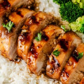 Sliced grilled honey garlic chicken breast plated with rice and broccoli.