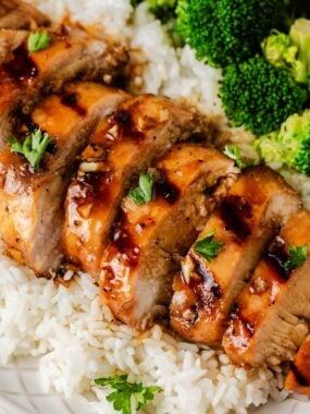 Sliced grilled honey garlic chicken breast plated with rice and broccoli.