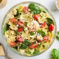 Pesto pasta salad with chicken in clear serving bowl.