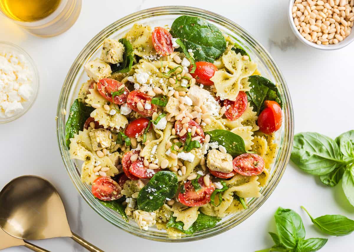 Pesto pasta salad with chicken in clear serving bowl.