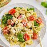 Pesto pasta salad with chicken on a white plate with gold fork.