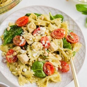 Pesto pasta salad with chicken on a white plate with gold fork.
