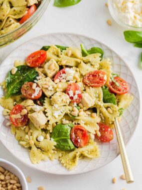 Pesto pasta salad with chicken on a white plate with gold fork.