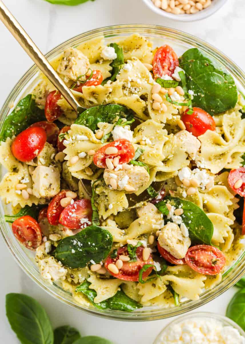 Pesto pasta salad in a bowl with gold serving spoon.
