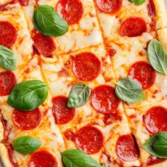 Sliced puff pastry pizza topped with pepperoni and fresh basil leaves on a parchment-lined baking sheet.