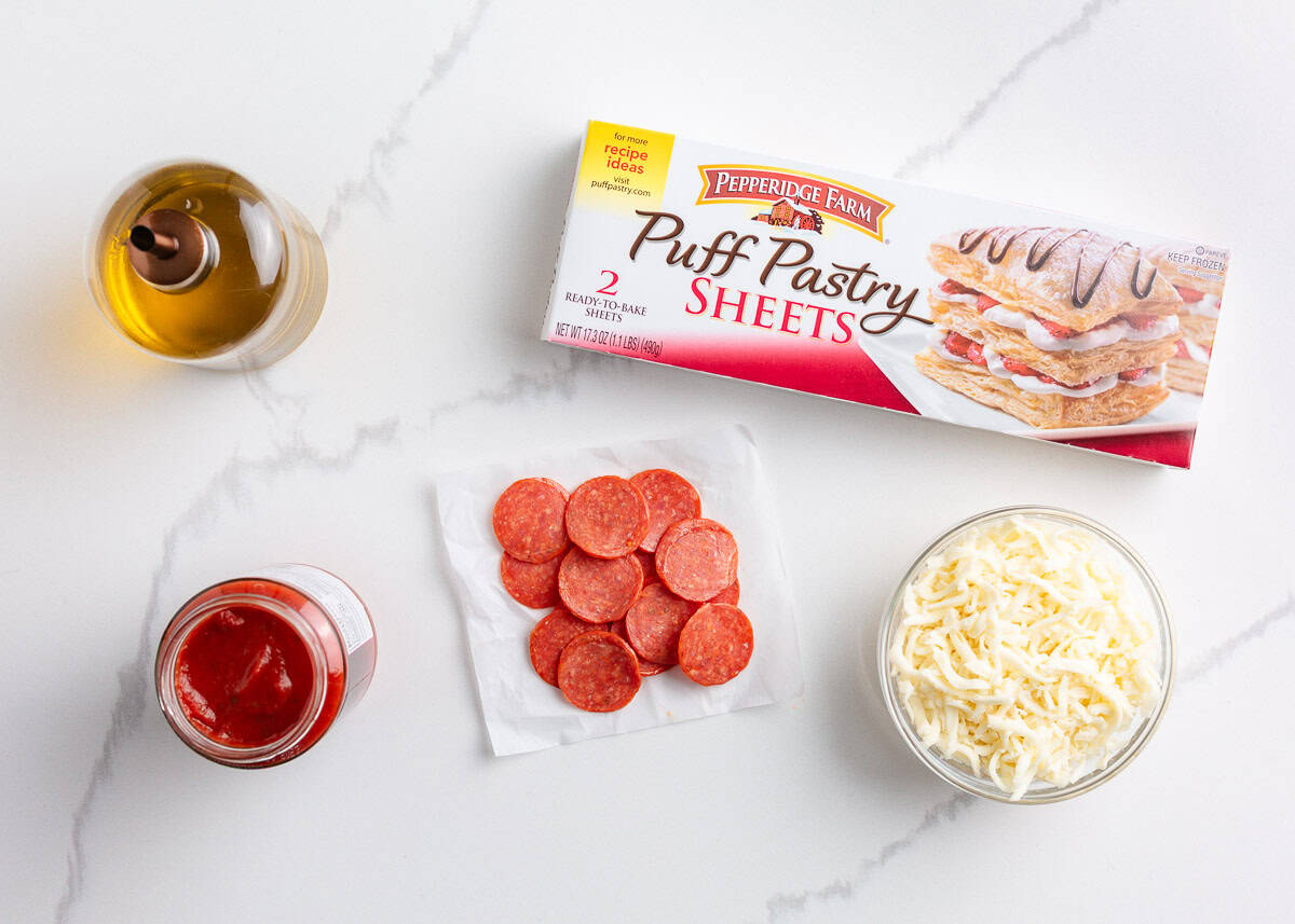 Puff pastry, pepperoni, pizza sauce and cheese on counter. 