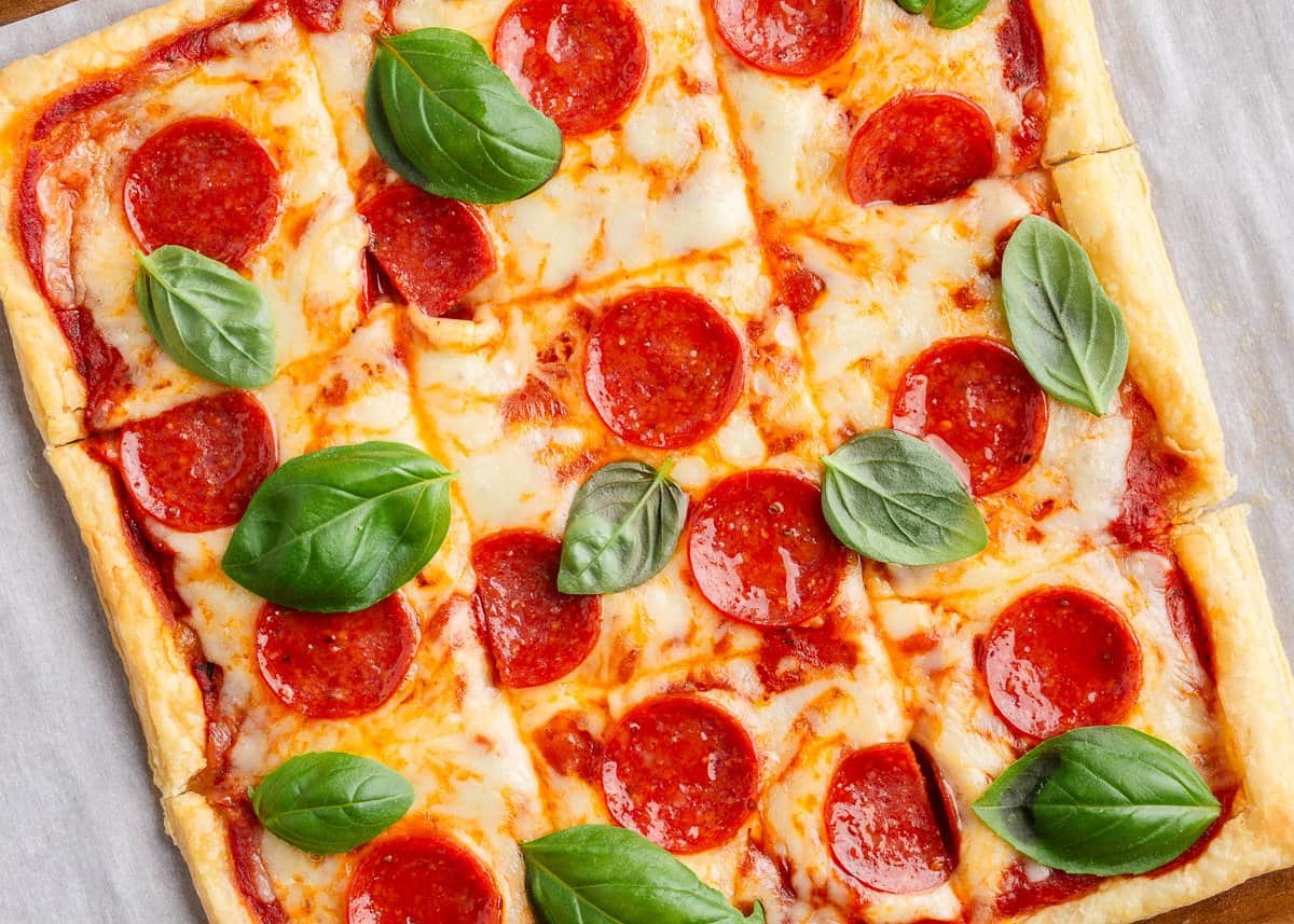Puff pastry pizza with pepperoni and basil on parchment paper lined baking sheet. 