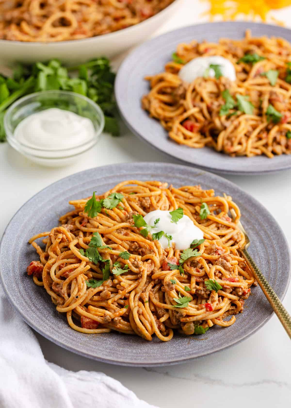 Two plates of taco spaghetti topped with sour cream and cilantro. 