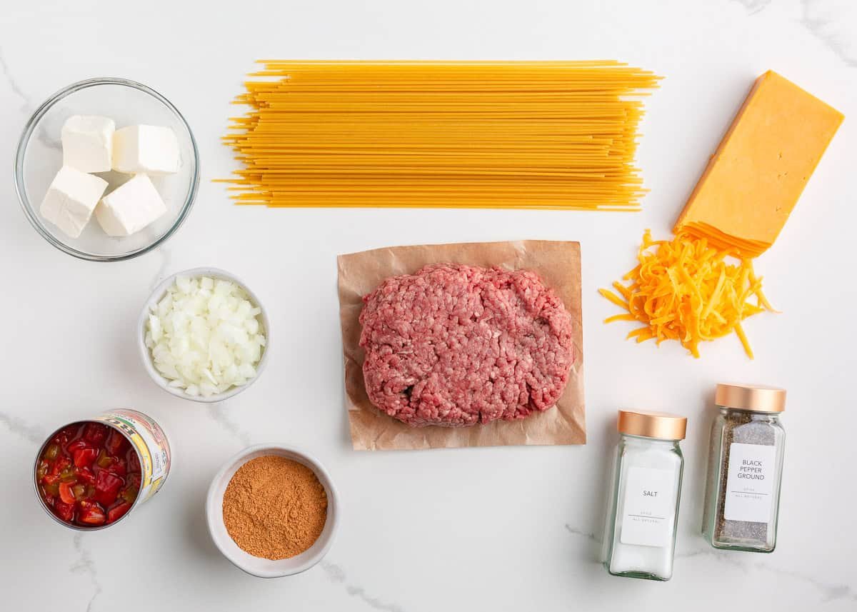 Flat lay of ingredients for taco spaghetti including pasta, ground beef, shredded cheese, cream cheese, taco seasoning, and diced rotel tomatoes.